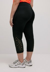 Zwarte capri legging met een hoge taille, voorzien van een textuurpatroon van stippen in een lichtere tint aan de zijkanten, gemaakt van rekbare stof.
