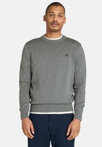 Grauer Pullover mit Rundhalsausschnitt, gerippten Bündchen und Saum, mit einem kleinen Logo auf der Brust. Der Stoff wirkt weich und strukturiert.