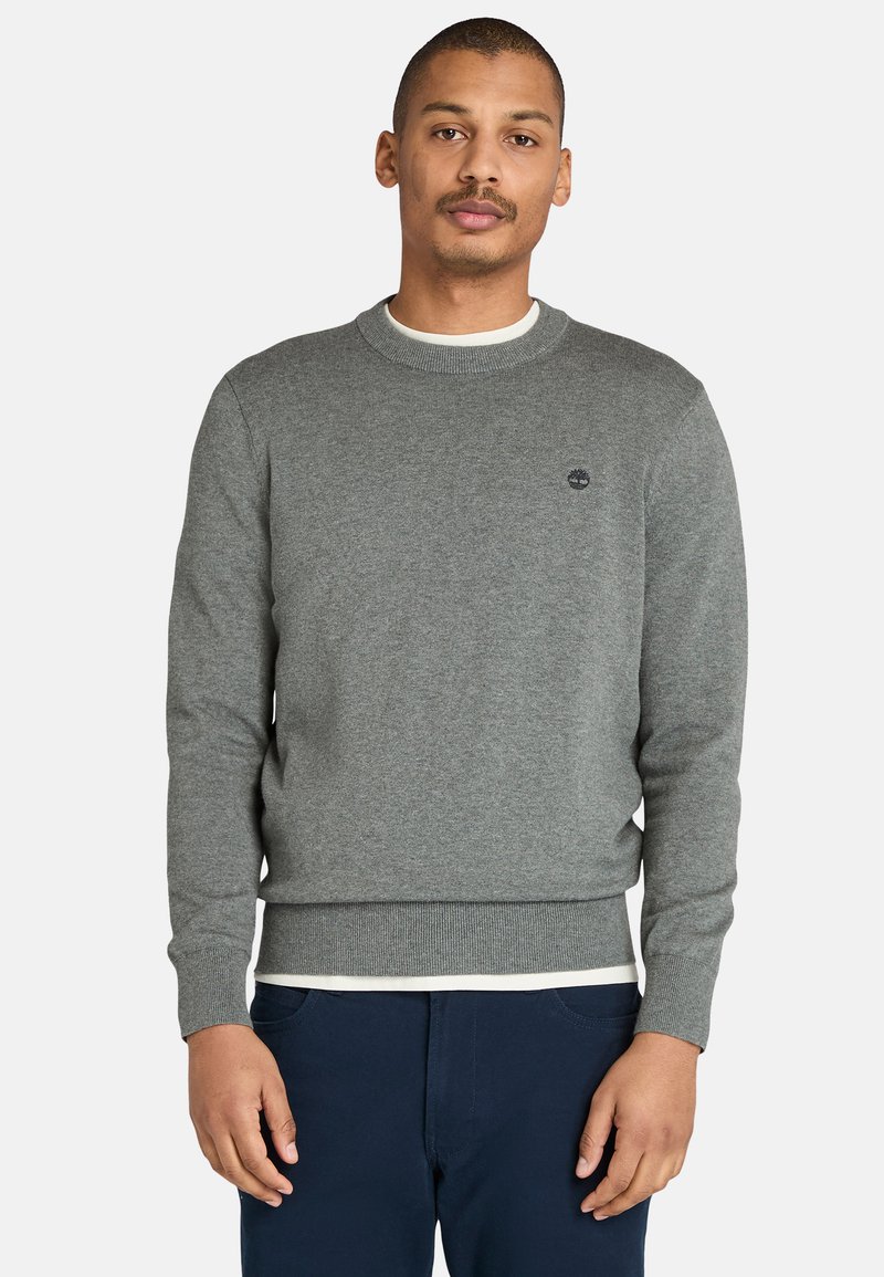 Grauer Pullover mit Rundhalsausschnitt, gerippten Bündchen und Saum, mit einem kleinen Logo auf der Brust. Der Stoff wirkt weich und strukturiert.