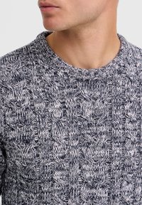 Gray and white knitted sweater featuring a thick cable pattern, crew neck design, and textured fabric. Close-up view of neckline and pattern details.