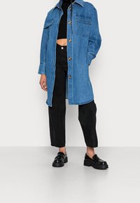 Kurtka dżinsowa w jasnoniebieskim kolorze, zapinana na guziki, z dwoma kieszeniami na piersi, zestawiona z czarnymi spodniami o szerokich nogawkach oraz masywnymi czarnymi butami.