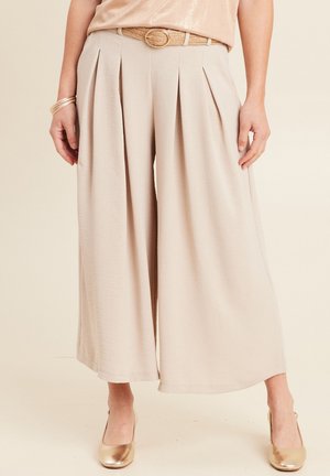 Beige wijde pijpen broek met voorplooien, gemaakt van lichte stof, gecombineerd met een gevlochten riem en gouden schoenen. Contrast met een glanzend top.
