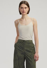 Top sin mangas beige con tirantes delgados, combinado con pantalones de pierna ancha verde oliva que presentan bordados florales y detalles de botones.