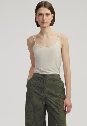 Top sin mangas beige con tirantes delgados, combinado con pantalones de pierna ancha verde oliva que presentan bordados florales y detalles de botones.