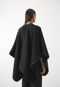Svart ullponcho med avrundet kant, sømløs design og en glatt tekstur. Utringningen er enkel og formet for komfort.