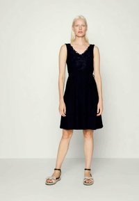 Vestido sem mangas azul-marinho com decote em V, bordado floral no corpete e saia evasê. Modelo usa sandálias de cor clara.