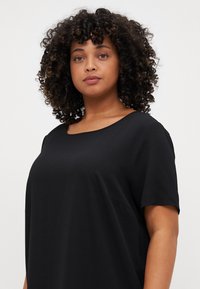 Haut noir à manches courtes avec un col rond, fabriqué à partir d'un tissu texturé, présentant des coutures latérales discrètes et une coupe décontractée.