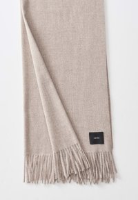 Sciarpa rettangolare beige realizzata in morbido tessuto, con bordi frangiati e un'etichetta nera cucita in un angolo. Tessuto liscio.