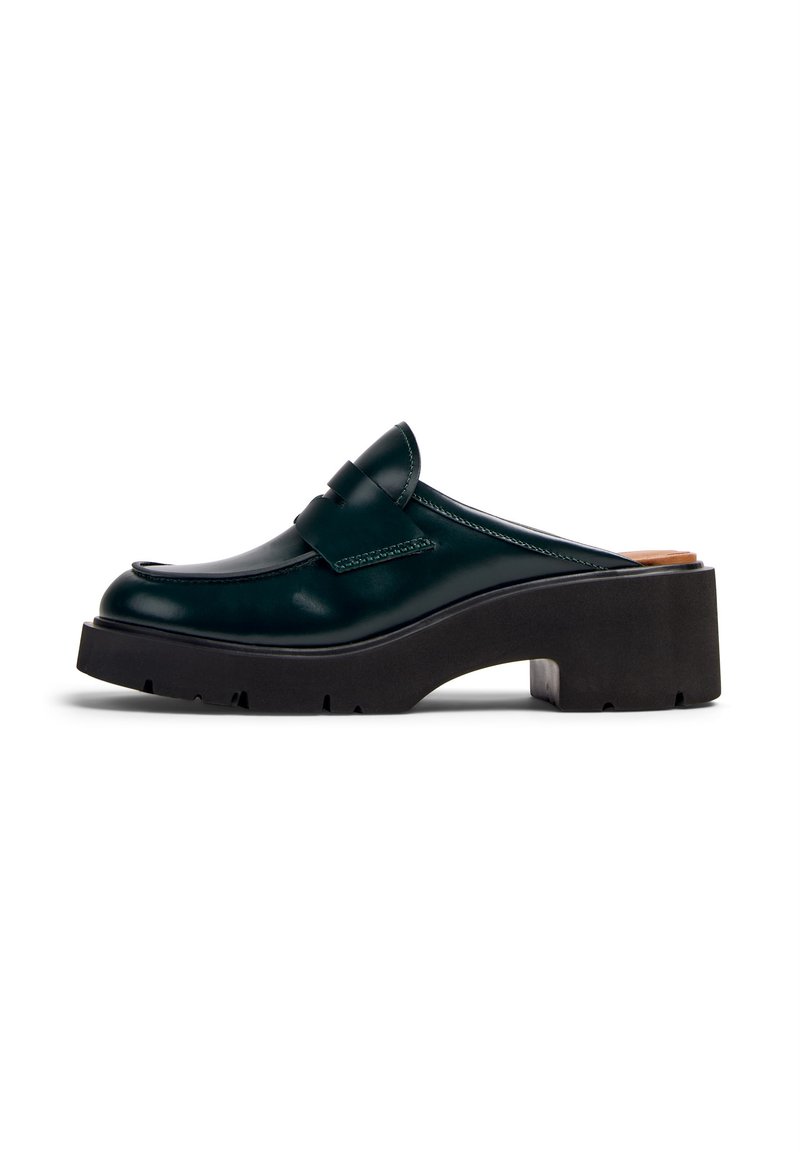 Zoccolo in pelle verniciata verde con punta arrotondata, dotato di una cinghia decorativa e una suola piatta nera chunky con una superficie testurizzata.
