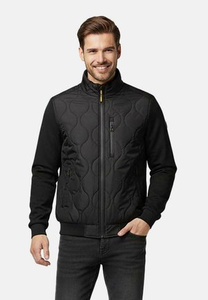 Zwarte doorgestikte jas met een hoge kraag, ritssluiting aan de voorkant en getextureerde panelen. Heeft zijzakken en geribbelde manchetten en zoom.