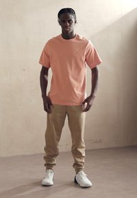 T-shirt pêche à manches courtes avec un col rond, pantalons beiges et chaussures de sport blanches. Design simple, tissu lisse et coupe décontractée.