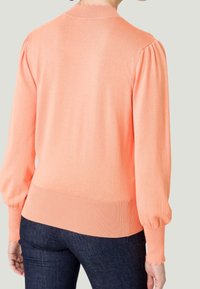 Licht koraalkleurig cardigan met ribgebreide manchetten en onderrand, met pofmouwen en een gegolfde halslijn. Gemaakt van een zachte gebreide stof.