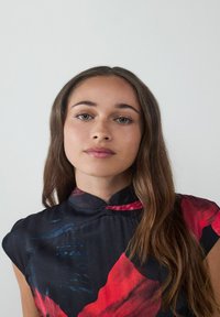 Vestido sin mangas de patrón negro y rojo con cuello alto, textura suave y diseños abstractos. Tela suave con un brillo visible.