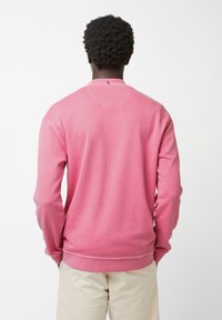 Sudadera rosa con cuello redondo y mangas largas. Textura suave con puños y dobladillo acanalados, detalles de costura visibles en el cuello.