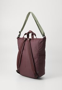 Bolso de hombro burdeos con correa ajustable verde, dos asas superiores de transporte, textura acolchada y bolsillos laterales para almacenamiento.
