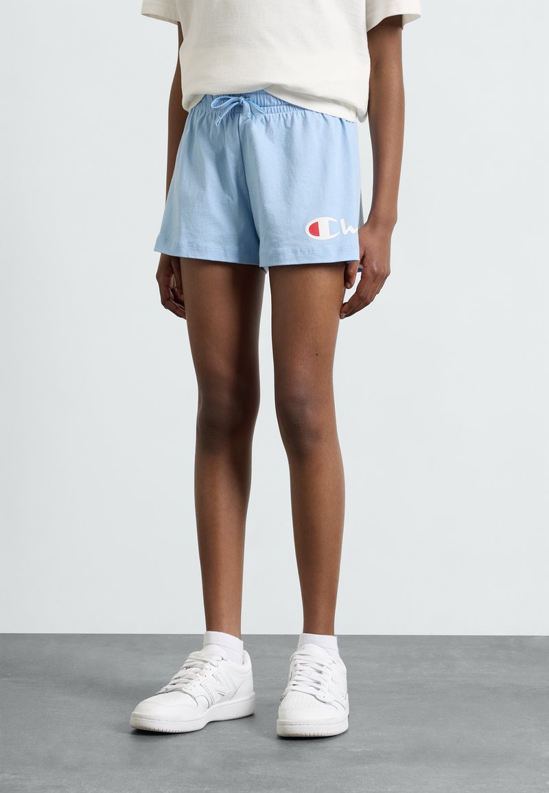 Shorts en coton bleu clair avec une taille élastique et un cordon de serrage, arborant un logo blanc et rouge sur le côté gauche.