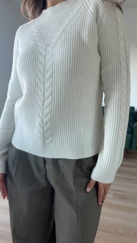 Witte gebreide trui met een gestructureerd kabelbreipatroon, ronde hals en geribbelde manchetten. Gecombineerd met grijze, op maat gemaakte broek.