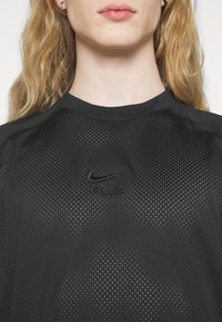 Svart mesh-träningsskjorta med rund halsringning, med perforerad textur och en diskret svart Nike Air-logotyp på framsidan.
