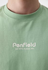 Világoszöld pamut póló, kerek nyakkivágással. Középen elhelyezett fehér szöveg olvasható: "PenField" és "Est 1975. Hudson, MA."