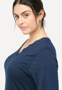 Tmavě modré tričko s výstřihem do V, s krajkovými detaily kolem límce. Měkká tkanina a krátké rukávy, přizpůsobený střih.