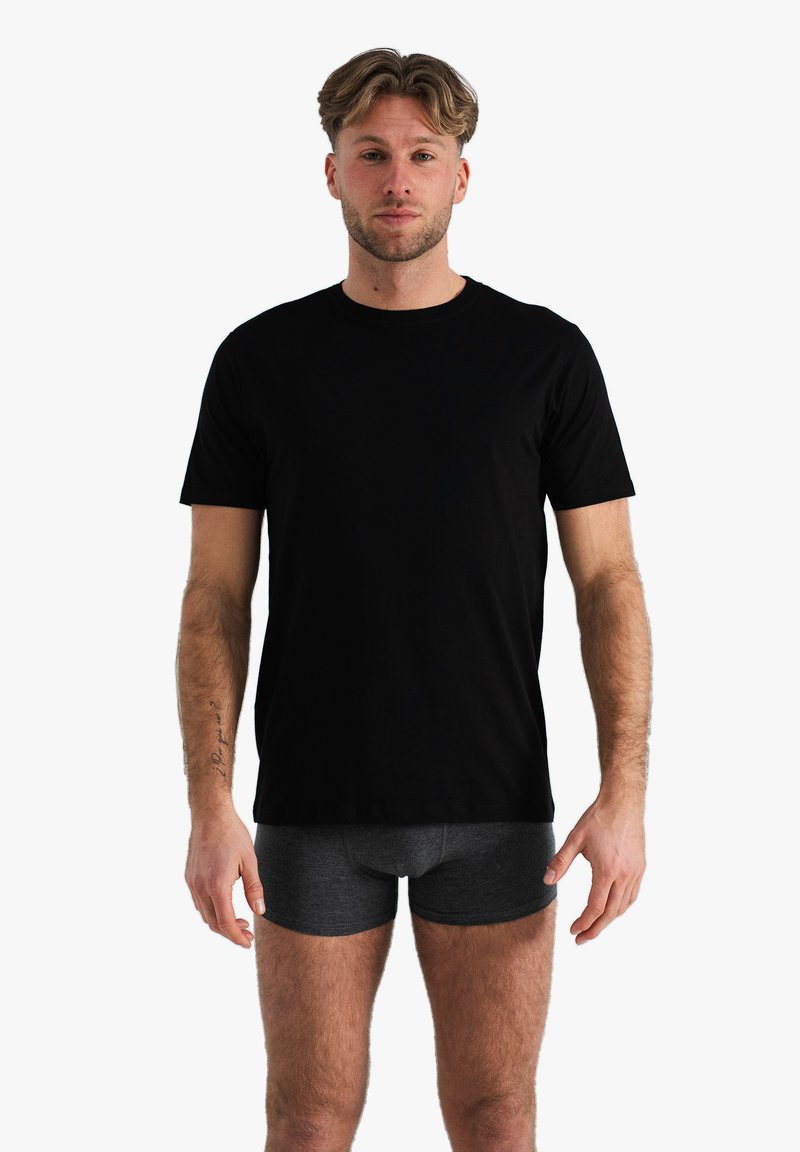 T-shirt en coton noir avec un col rond et des manches courtes, porté avec un short boxeur gris foncé. Texture lisse, coupe légèrement décontractée.