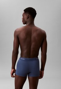 Boxer briefs blu navy realizzati in materiale morbido, con un elastico in vita personalizzato. Modello mostrato di spalle su uno sfondo grigio.