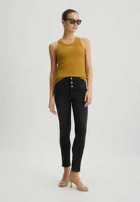 Canottiera a coste senape con piccolo logo, abbinata a jeans neri a vita alta con cinque bottoni e sandali con tacco metallici e con fasce.