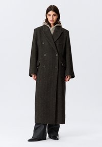 Long, dark green double-breasted coat with textured fabric, large lapels, two front pockets, and contrasting grey inner lining.