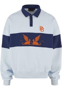 Langermet polo sweatshirt i lyseblå og marine, med oransje brodert logo og vinget griffin-design over brystet.