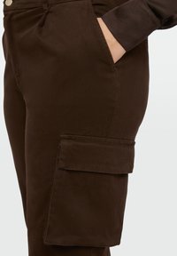 Bruine cargobroek met een zijzak, gemaakt van een soepele stof met een getailleerde pasvorm en een klassiek taillebandontwerp.