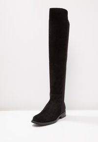 Svart just-over-kneet stövel i mocka med en slät yta, något rundad tå och låg blockklack. Enkel, stilren design utan synlig hårdvara.