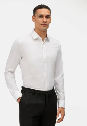 White long-sleeve dress shirt with a spread collar and button closure, paired with black trousers. Smooth fabric and tailored fit.