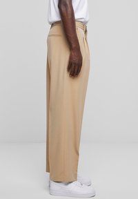 Beige wijde broek van lichtgewicht stof, met plooien en zijzakken, gedragen met witte sneakers.