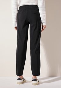 Pantalons noirs ajustés avec une taille élastique, deux poches arrière et une finition en tissu lisse. Assortis à des baskets blanches avec un logo.