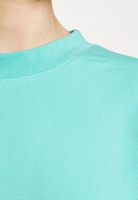 T-shirt turchese con collo a girocollo realizzato in cotone morbido, caratterizzato da una texture a coste e un delicato dettaglio di cucitura attorno all'apertura del collo.