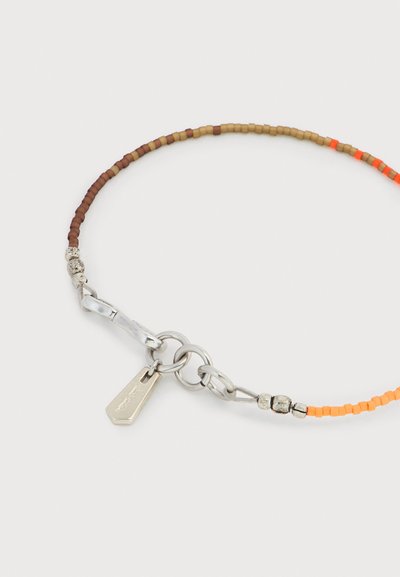 Βραχιόλι με χάντρες μικρές τετράγωνες σε αποχρώσεις καφέ, ταμπά και πορτοκαλί, με ασημένιο κούμπωμα και μια μικρή ορθογώνια ετικέτα.