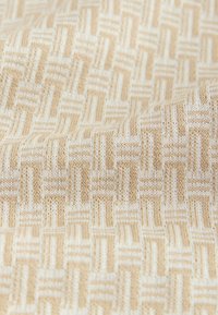 Bež in bela pletena tkanina z ponavljajočim se geometrijskim vzorcem prepletajočih se pravokotnih oblik, mehko zložena.