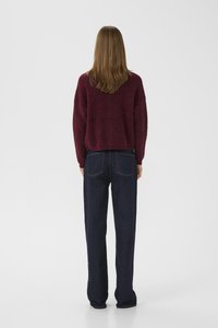Burgunderfarget strikkegenser og mørkeblå vidbenede jeans. Genseren har en avslappet passform; jeansene har baklommer og en klassisk denimtekstur.