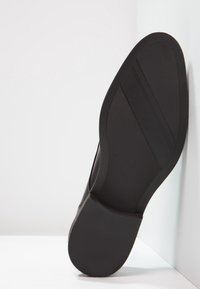 Semelle de chaussure noire avec surface en caoutchouc texturé. Présente une forme courbée et des rainures de conception pour une meilleure adhérence. Apparence propre et minimaliste.
