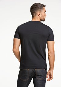 T-shirt nera a maniche corte, in cotone, design aderente, texture liscia, scollatura rotonda, indossata con jeans scuri, vista da dietro.