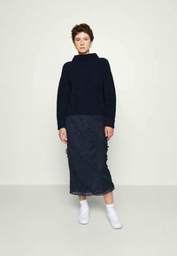 Mornarsko plavi rebrasti turtleneck pulover u kombinaciji s lepršavom mornarsko plavom suknjom s valovitim volanima. Uparen s bijelim tenisicama.
