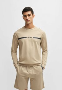Beige long-sleeve shirt with a black "BOSS" logo and two horizontal black stripes. Paired with matching beige shorts with a relaxed fit.