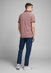 Rode en marineblauwe gestreepte polo met korte mouwen, gecombineerd met donkerblauwe jeans en witte sneakers. Glad textuur, casual pasvorm.