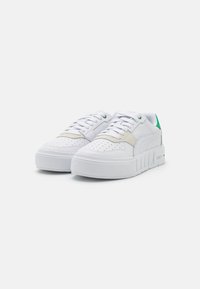 Hvide sneakers med en tekstureret sål, der har en cremefarvet accent på den ene side, en grøn hælflap og perforerede detaljer på tæerne.