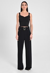 Top nero accorciato con spalline spesse e scollatura a cuore, abbinato a pantaloni neri a gamba larga con vita alta e una cintura statement.