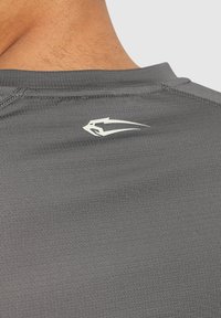 Grau athletisches T-Shirt mit glatter Textur, Nähdetails und einem weißen Logo auf der Rückseite in der Nähe des Ausschnitts.