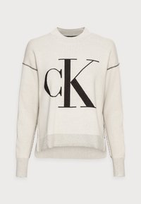 Sweter w kolorze kremowym z wyraźnym czarnym logo "CK", z wysokim kołnierzem i bocznymi suwakami. Ściągacze na rękawach i u dołu.
