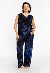 Schwarzes Outfit mit blauem Blumenmuster; ärmelloses Top mit gerafftem Dekolleté, kombiniert mit weiten Hose; glattes Material und fließendes Design.