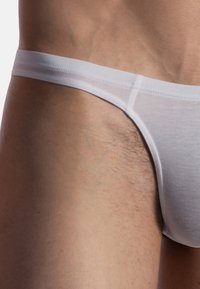 Weißer Tanga aus weichem, dehnbarem Material. Verfügt über einen schmalen Bund und eine glatte Textur, die minimale Abdeckung bei einer engen Passform bietet.