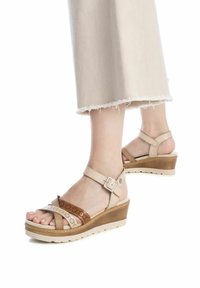 Sandalias de cuña beige y marrón con parte superior texturizada, cuentan con una correa de tobillo ajustable y un diseño perforado. Suela ligera, estilo casual.